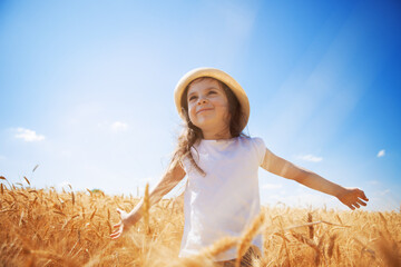 Happy girl walking in golden wheat, enjoying the life in the field. Nature beauty, blue sky and...