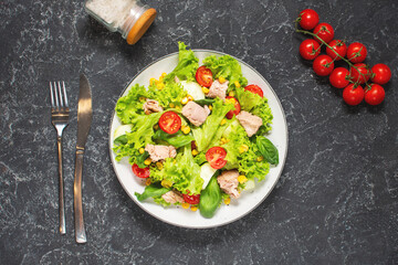 Tuna Fish Salad with Lettuce, Cherry Tomatoes, Cucumber and Corn on black stone background