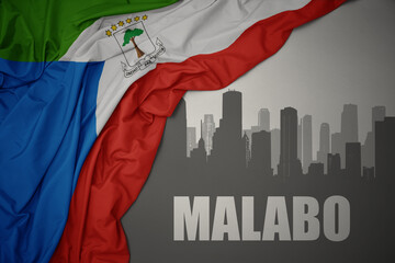 abstract silhouette of the city with text Malabo near waving colorful national flag of equatorial guinea on a gray background.
