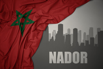 abstract silhouette of the city with text Nador near waving colorful national flag of morocco on a...