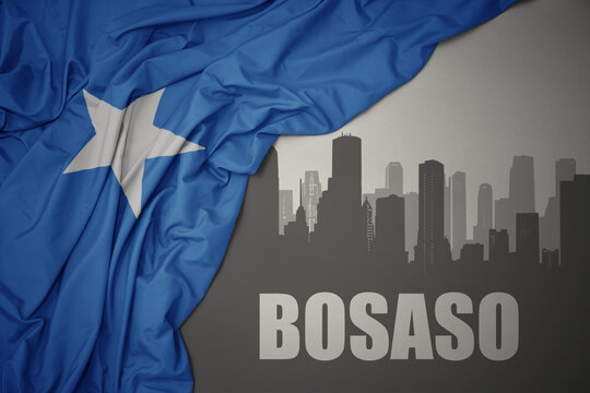 abstract silhouette of the city with text Bosaso near waving colorful national flag of somalia on a gray background.