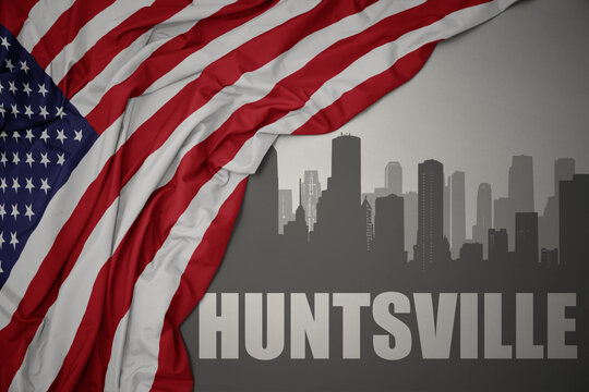 abstract silhouette of the city with text Huntsville near waving colorful national flag of united states of america on a gray background.