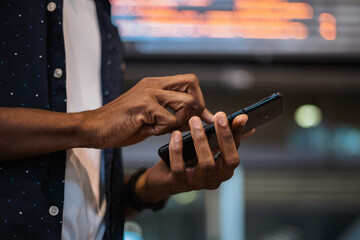 Close up shot of african man sending a text message on the phone. He is at a train station.