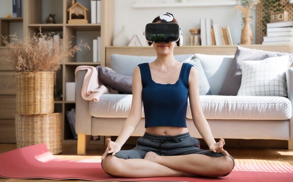 Young Asian female doing yoga in VR glasses at home