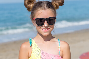 A young girl applies sunscreen to her body on the beach.