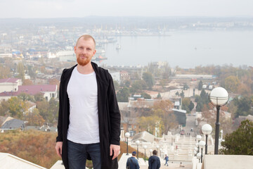 A young man with a red beard against the backdrop of a staircase and an autumn landscape