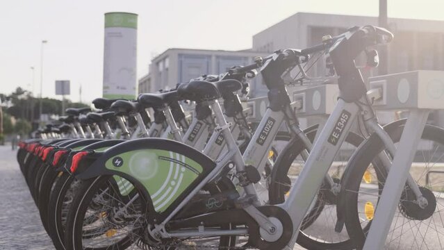 Bicycle rental service on city road. Public green transportation.  New bike sharing system along the streets of the city. Group of grey bikes ready to use. Portugal, Lisboa. July 16, 2022.