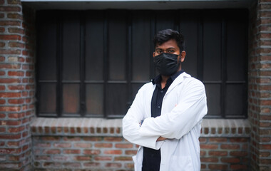 South asian young confident male doctor in white apron and black face mask, Bangladeshi muslim medical student, protection from corona virus and flu viruses