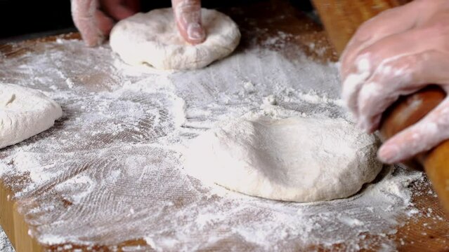 Human hands roll out fresh dough for make bread or pizza on kitchen board for baking.