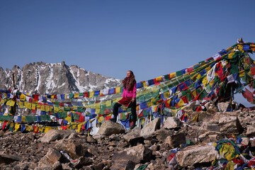 woman standing on top of  high pass in Himalayan mountains marked with Buddhist flags - obrazy, fototapety, plakaty