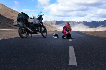 Woman sitting on asphalt road near her motorcycle in high mountains of Himalayas