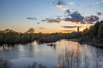 Rural landscape with a river at sunset. Evening in early spring in May. The sun is above the horizon, shining through the clouds.