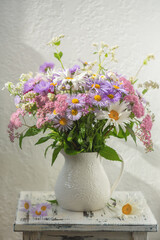 Summer bouquet of garden flowers with chamomile and Aster alpinus in a white jug