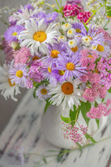 Summer bouquet of garden flowers with chamomile and Aster alpinus in a white jug