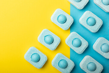 Water softener tablets on yellow-blue background, flat lay. Space for text.Capsules for washing machines and dishwashers that prevent limescale. Place to copy.