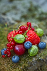 Summer blueberries, strawberries, gooseberries and red currants on an old stone background. Soft, selective focus.