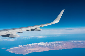 Fototapeta premium Aerial window view from an airplane on Fuerteventura, Canary Islands, Spain, Europe, EU. Wing and turbines of the aircraft can be seen. Flying high above the ground. Freedom. Flying into vacation