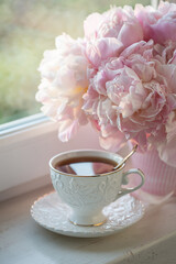 Cup of tea with pink peonies in a vase
