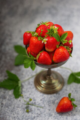 Ripe strawberries in an old silver vase on a gray background.
