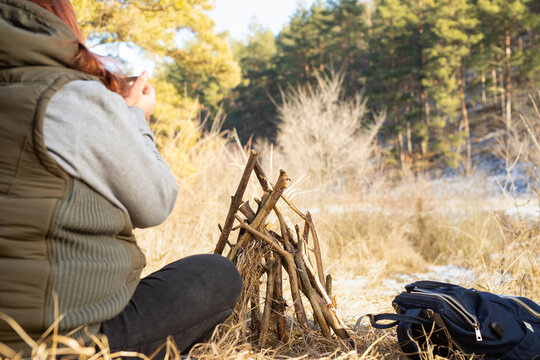 Back vie photo of a fat traveler woman sitting in front of the forest with bonfire and backpack near drinking hot tea.