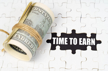 Dollars lie on white puzzles, on a black surface there is an inscription - Time to Earn