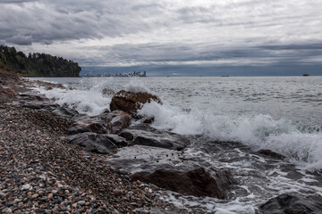 Sea waves crashing the rocky seashore with a city view on the background