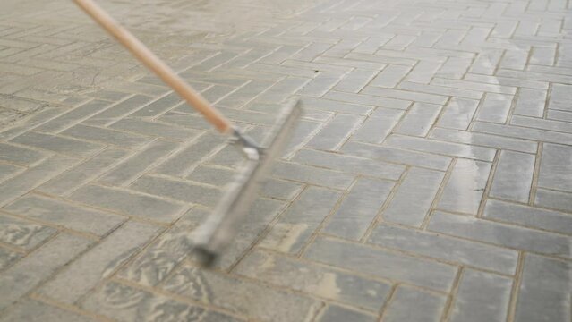 The concept of laying paving stones. A worker using a mop rubs the sand into the seams of the paving stones. A worker washes sand from freshly laid paving stones. A worker cleans the paving stones fro
