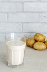 A transparent glass with potato milk on the table. A new trend in eating healthy. Alternative food concept. Vegetable Milk for Vegans. Vertical orientation. Selective focus