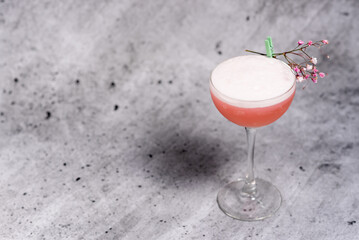 Beautiful caral color cocktail decorated with a flower on a concrete background. Long stem glass....
