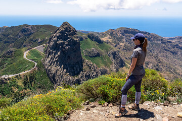 Fototapeta premium Woman with scenic view on mountain road next to volcanic rock formation Roque de Agando in Garajonay National Park on La Gomera, Canary Islands, Spain,Europe. Seen from lookout Mirador Morro de Agando