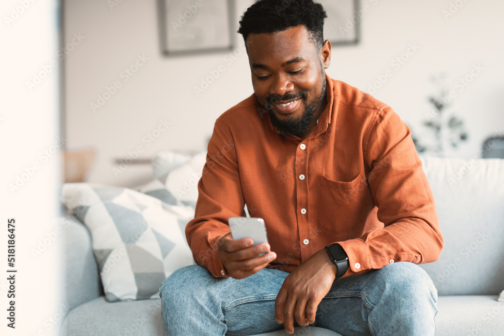 Poster happy black man using cellphone browsing internet texting at home