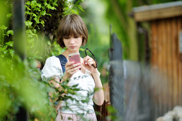 Obraz premium Pretty teenage girl using a smart phone. Cute young girl having fun during forest hike on beautiful summer day.