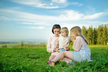 Two sisters and their toddler brother having fun outdoors on sunny summer day. Children exploring...