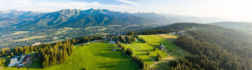 Aerial view of Zakopane town underneath Tatra Mountains taken from the Gubalowka mountain range. High mountains and green hills in summer or spring.