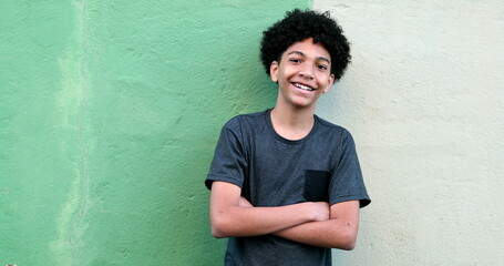 Young boy standing outside with arms crossed observing. Mixed race child black ethnicity smiling