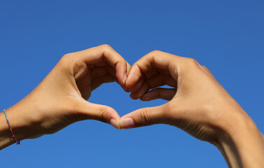 joined hands of a person forming a big heart and the blue sky background