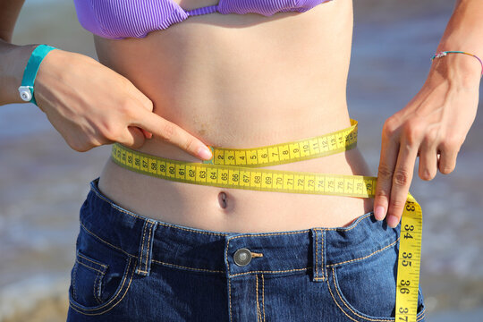 thin girl who measures her waist with the flexible measuring tape and shows her navel
