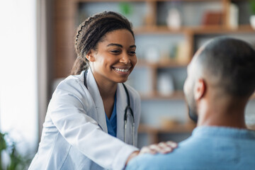Cheerful african american woman doctor touching male patient shoulder - obrazy, fototapety, plakaty