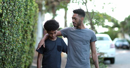 Two brothers walking together in sidewalk. Black brother giving advice to younger sibling