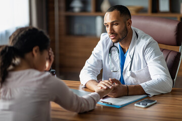Doctor having conversation with upset black woman patient, holding hand