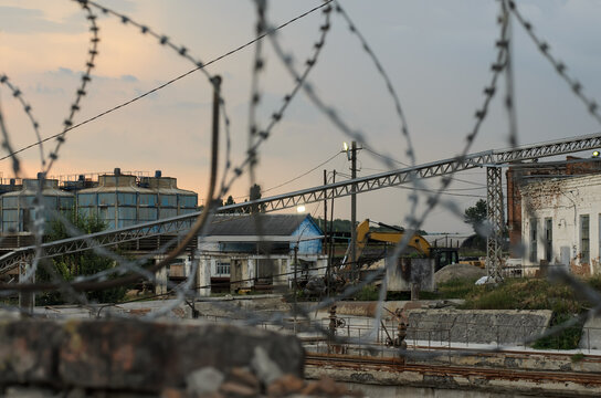 Industrial view of an old working sugar factory with old buildings and technological equipment, barbed wire in the foreground, cloudy evening sky, selective focus