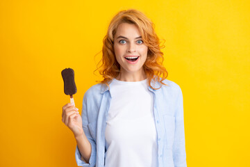 Photo of young woman eats delicious ice cream, enjoys frozen dessert, dressed in casual clothes, isolated on yellow background. Amazed surprised woman face.