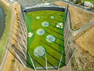 Aerial view of fenced golf driving range with high tech targets, rows of air conditioned hitting bays surrounded by high fence to stop golf balls