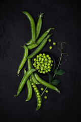 fresh green peas in pods and beans lie scattered on a plate and on a black plastered surface. top view. dark artistic flatley photo