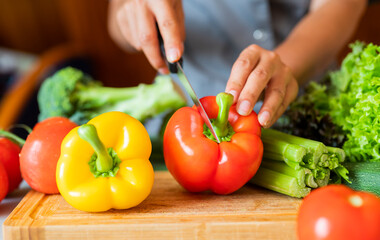 girl cook in the kitchen cuts red paprika with vegetables with a knife