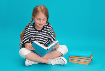 Child reading book sitting with legs crossed on blue background.
