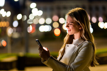 Beautiful young woman texting on the phone in the city at night.