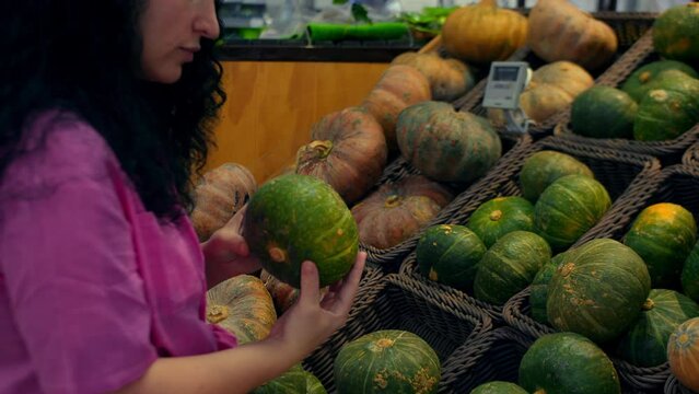 Young woman buys groceries, chooses a pumpkin in the supermarket for a Hollowin holiday. Attractive young girl in a pink suit chooses pumpkin vegetables at the vegetable market.