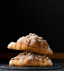 Baked croissant on a  board and sprinkled with powdered sugar, black table. Appetizing pastries for breakfast.
