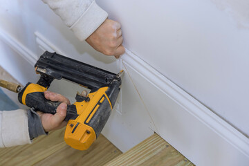 The carpenter uses a brad nail gun for the purpose of nailing the base molding trim on his new home
